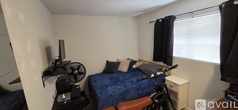 A small bedroom with a bed, a fan, a bicycle, and a television.