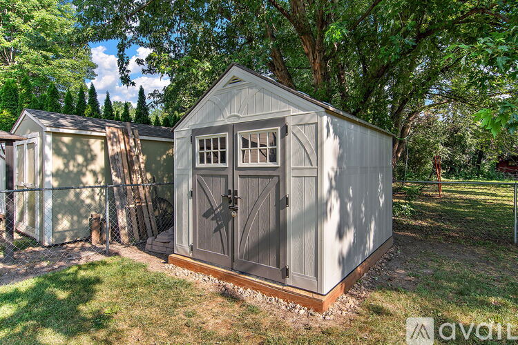 A grey shed with a brown door is surrounded by trees.