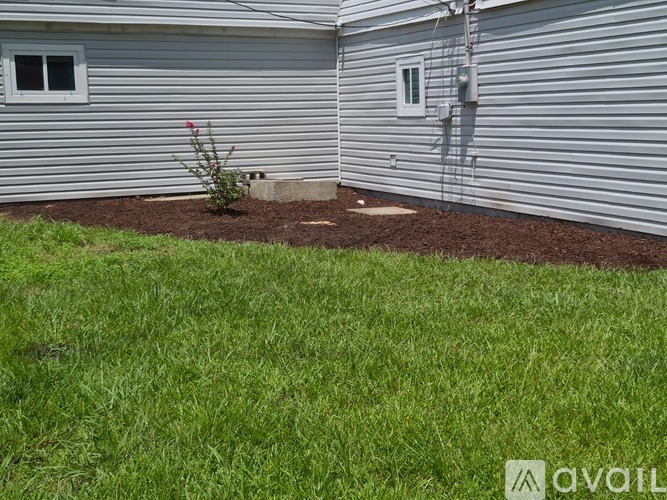 A small garden with a flower planted in the middle of a mulched area in front of a house.