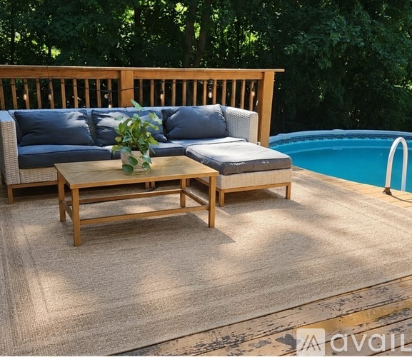 A wooden table with a vase of flowers on it sits on a patio next to a pool.