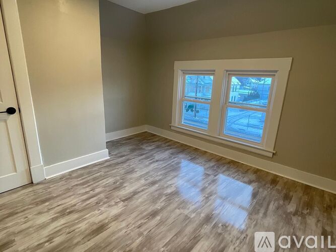 A room with a window showing a view of a house and trees outside.