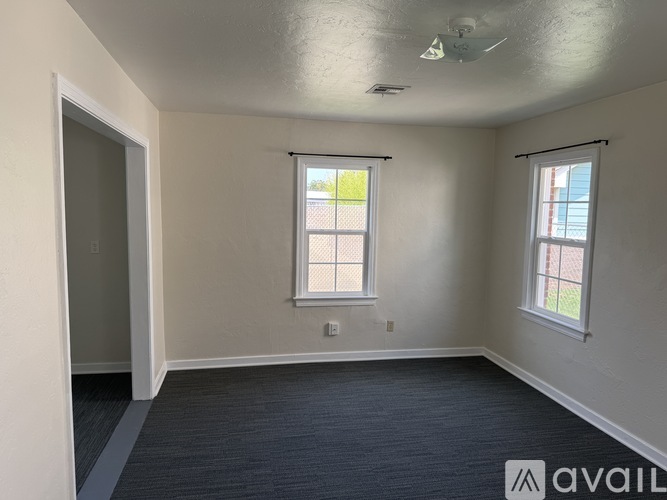 A room with a carpeted floor, two windows, and a ceiling fan.