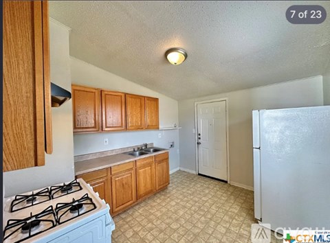 A kitchen with a white refrigerator, wooden cabinets, and a blue gas stove.