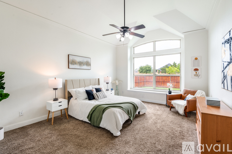 A bedroom with a large bed and a balcony overlooking a fence.
