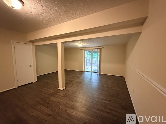 A spacious room with wooden flooring and a doorway leading to another room.