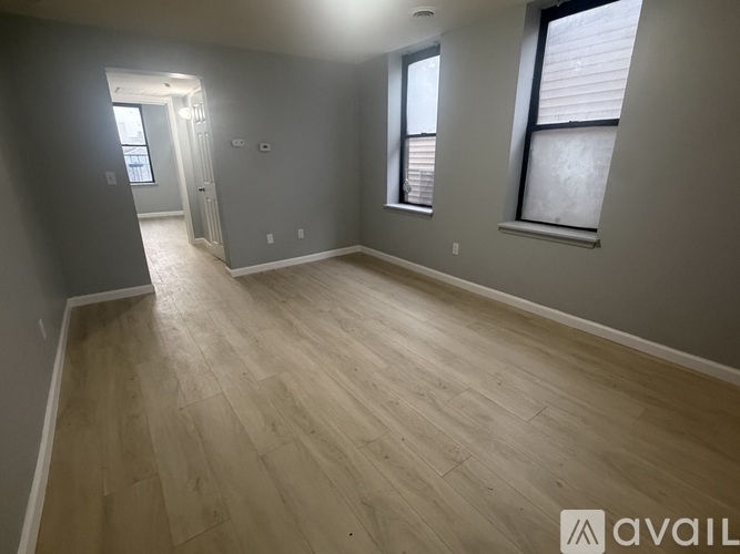 A room with wooden flooring and two windows.