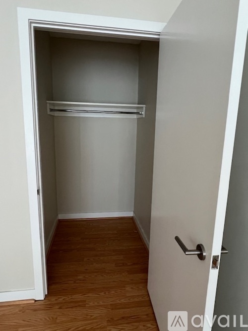A white door with a black handle is open to a small, empty room with a wooden floor.