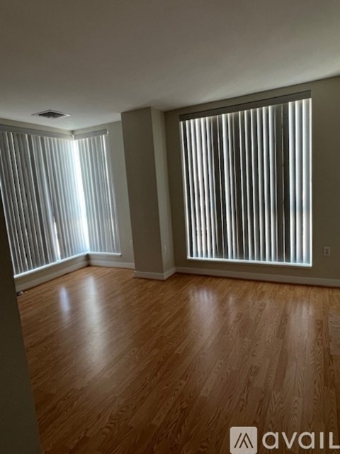 A room with wooden floors and two windows with vertical blinds.