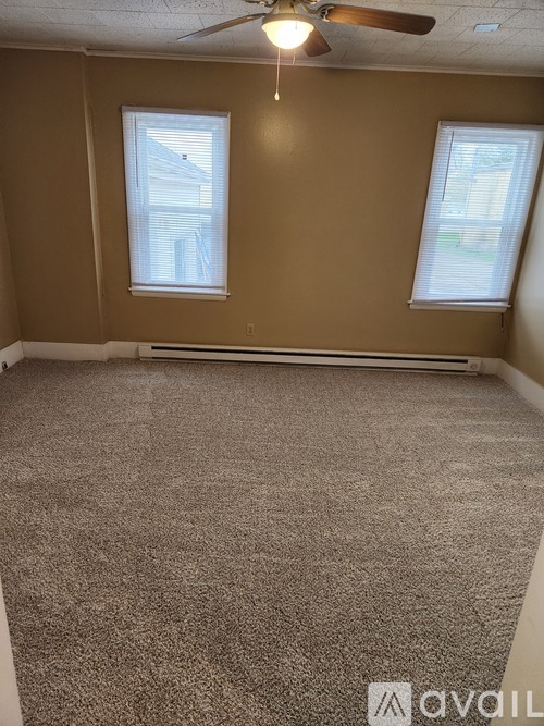 A room with a carpeted floor and two windows.