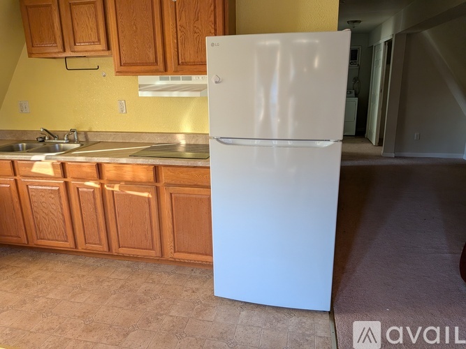 A white refrigerator stands in a kitchen with wooden cabinets.