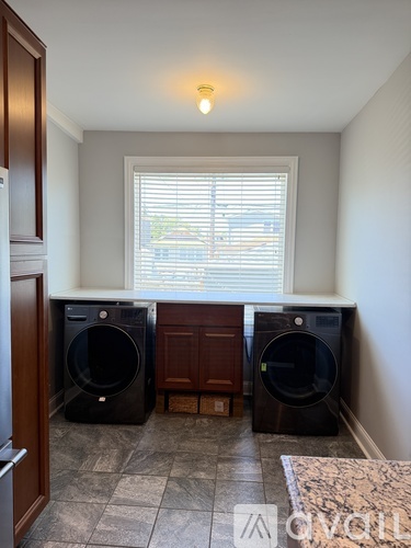 A laundry room with two washing machines and a window with blinds.