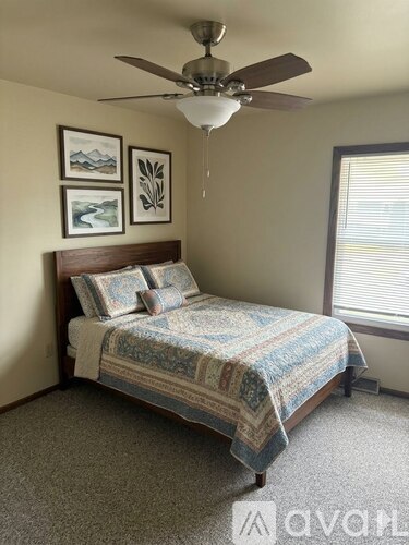 A bedroom with a bed, a ceiling fan, and two pictures on the wall.