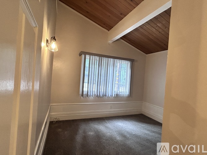 A room with a window covered by white blinds and a wooden ceiling.