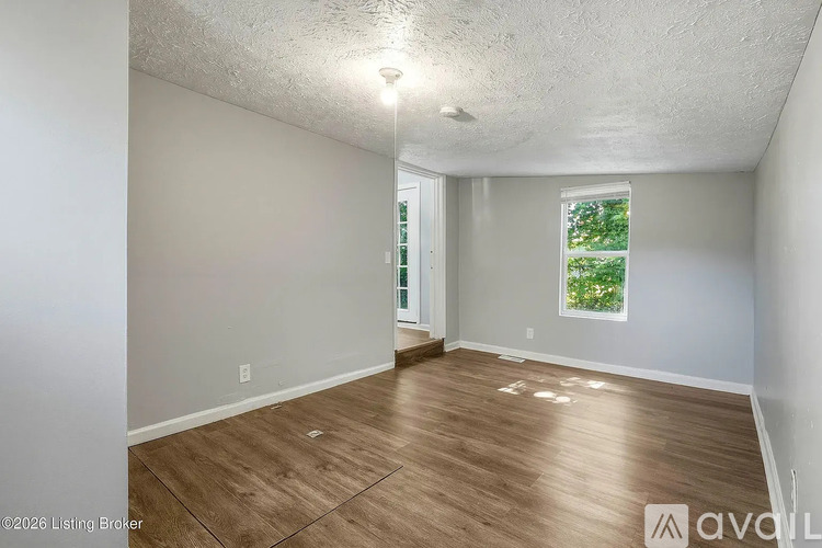 A room with wooden flooring and a window showing greenery outside.