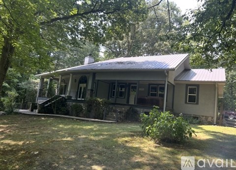 A house with a porch and a covered front door is surrounded by trees.