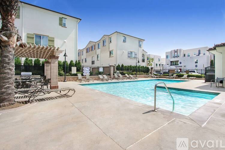 A swimming pool surrounded by a concrete patio and a white building with a balcony.