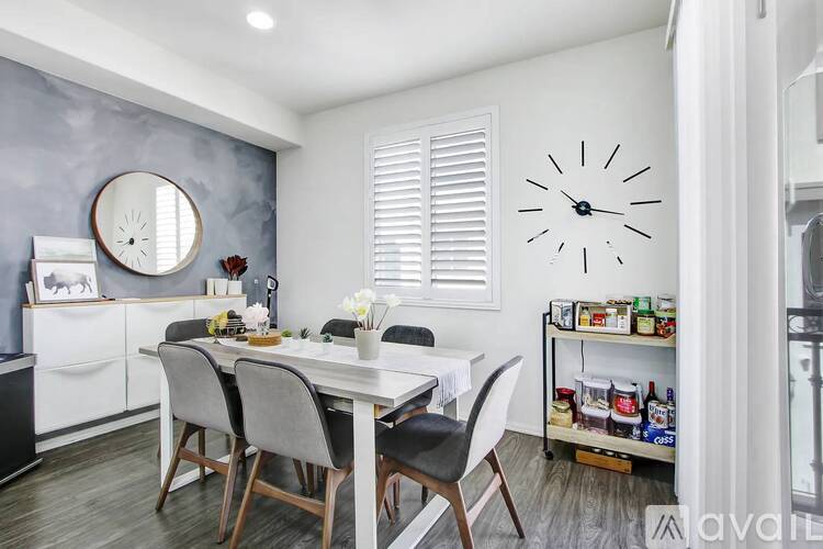 A dining room with a white table and chairs, a round mirror, and a large clock on the wall.