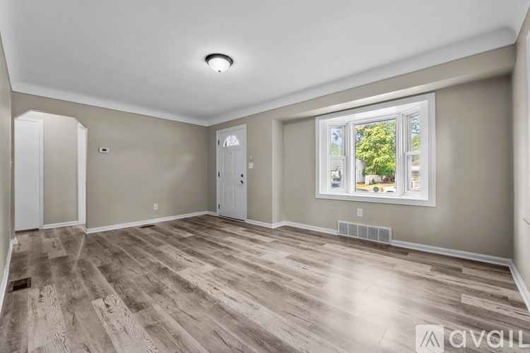 A room with wooden flooring and a window showing trees outside.