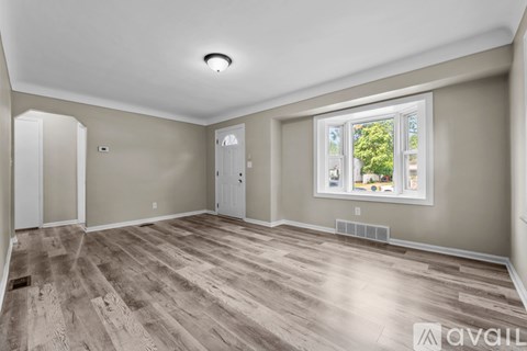 A room with wooden flooring and a window showing trees outside.
