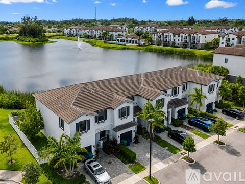 A large white house with a brown roof is surrounded by a lake and other houses.