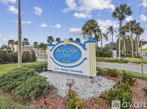 A sign for Boca Ciega Lane in a community with a blue sky and palm trees in the background.
