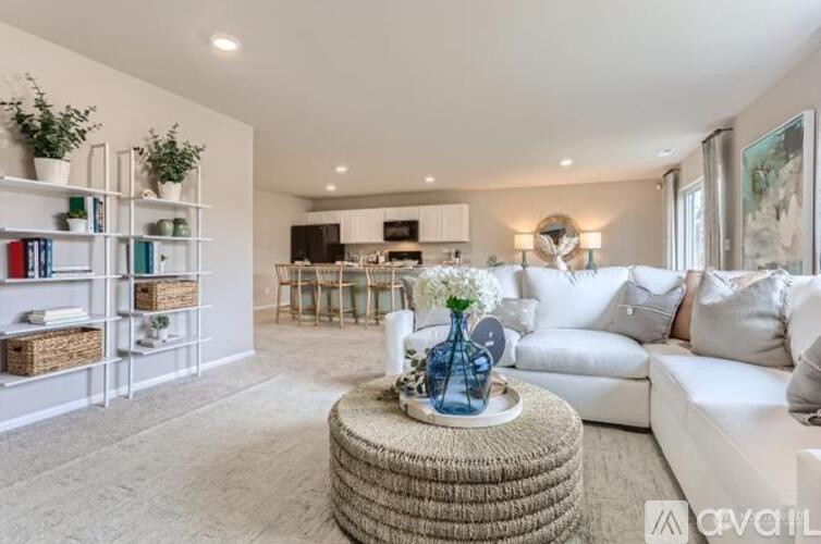 A living room with a white couch, a round wicker coffee table, and a bookshelf with plants on it.