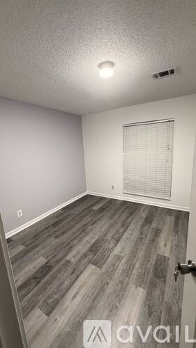 A room with a wooden floor and a window with blinds.