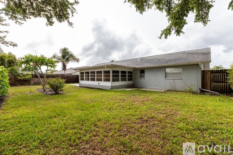 A house with a grey roof and a white wall is surrounded by a green lawn.