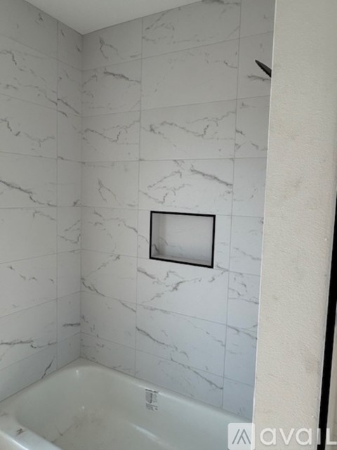 A bathroom with a marble tile wall and a white bathtub.