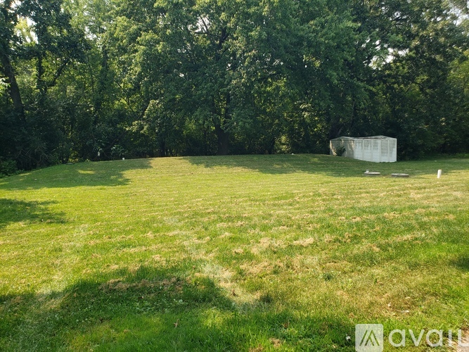 A grassy field with trees in the background and a white structure in the middle.