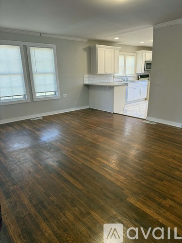 A room with wooden flooring and a kitchen area in the background.