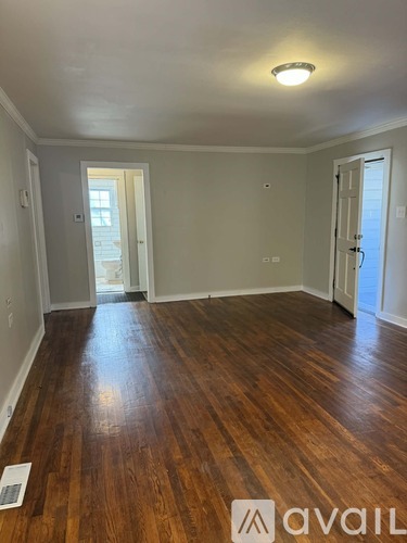 A room with wooden floors and white walls, with a door on the right and a window on the left.