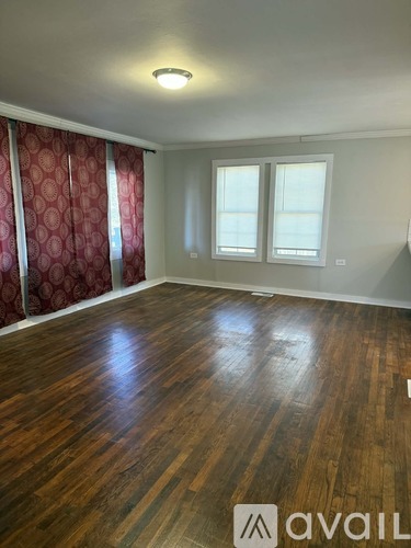 A room with wooden flooring and a window with a red curtain.