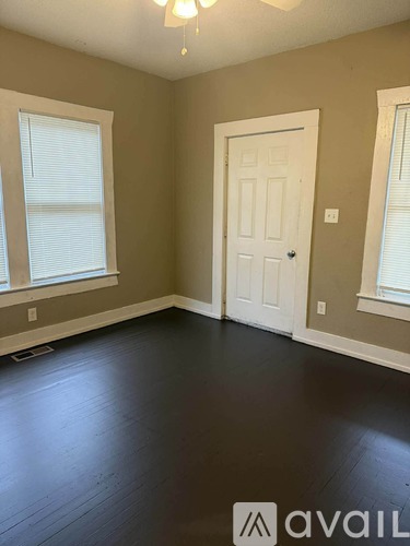 A room with a white door, two windows with blinds, and a chandelier.