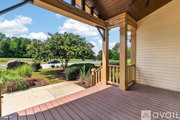 A wooden deck with a railing and a view of a green lawn and trees.