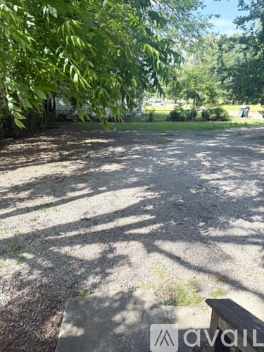 A gravel area with trees and a bench in the foreground.