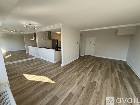 A spacious room with wooden flooring and a kitchen area in the background.