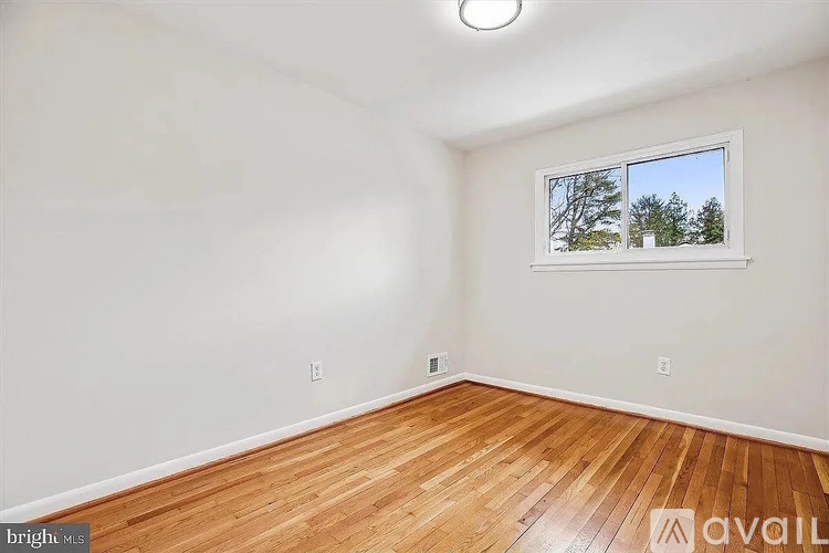 A room with wooden flooring and a window showing trees outside.