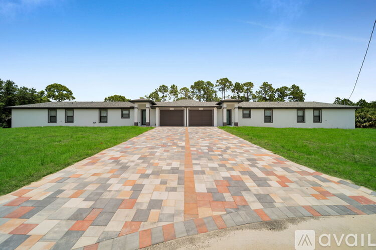 A long brick pathway leads to a white building with a brown door.