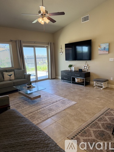 A living room with a grey sofa, a glass coffee table, a flat screen TV, and a ceiling fan.
