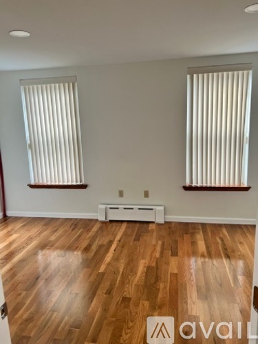 A room with wooden floors and two windows with blinds.