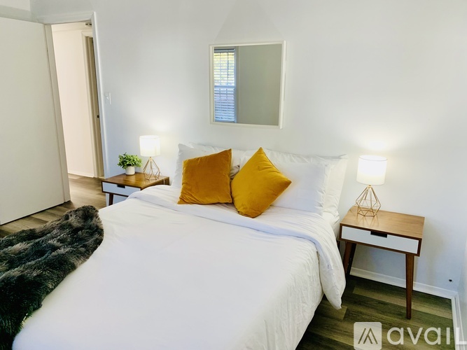 A bedroom with a white bed and a small table with a lamp on it.
