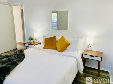 A bedroom with a white bed and a small table with a lamp on it.