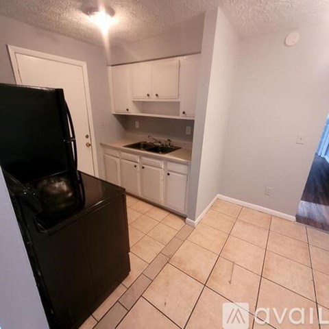 A black fridge sits in a kitchen with white cabinets and a stove.