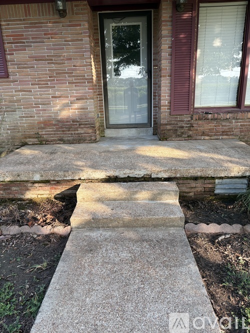 A brick house with a grey concrete walkway leading to the front door.