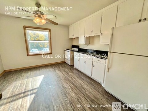 A well-lit kitchen with white cabinets and a window showing trees outside.