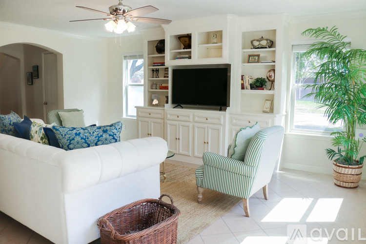 A living room with a white couch, a green striped chair, and a television on a cabinet.