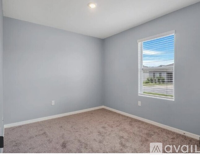 A room with a carpeted floor and a window showing a view of a house and trees.