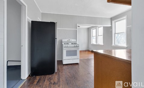 A kitchen with a black refrigerator, white oven, and wooden floors.