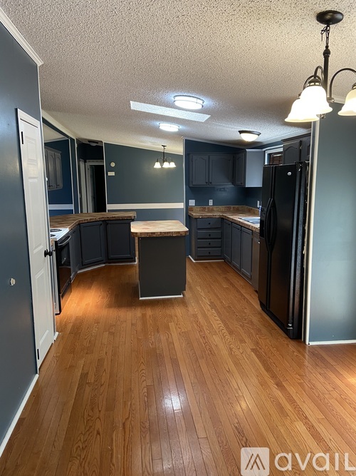A kitchen with wooden floors and a black refrigerator.